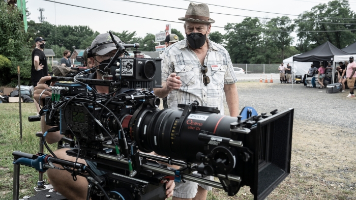 Behind-the-Scenes aus The Walking Dead: Daryl Dixon: Ein Kameramann arbeitet an einer großen Filmkamera, während ein Regisseur mit Hut und Maske daneben steht und Anweisungen gibt. Im Hintergrund sind Crewzelte und Filmmitarbeiter zu sehen.