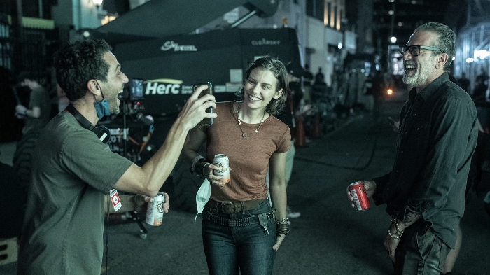 Behind-the-Scenes aus The Walking Dead: Dead City: Lauren Cohan (Maggie) und Jeffrey Dean Morgan (Negan) lachen mit einem Crewmitglied am Set. Alle halten Getränkedosen in der Hand, die Szene spielt sich nachts auf einer Straße ab.