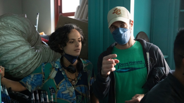 Behind-the-Scenes aus The Walking Dead: Dead City: Zwei Crewmitglieder mit Masken stehen in einem Set mit blauen Wänden. Einer zeigt in eine Richtung, während die andere aufmerksam zuhört.