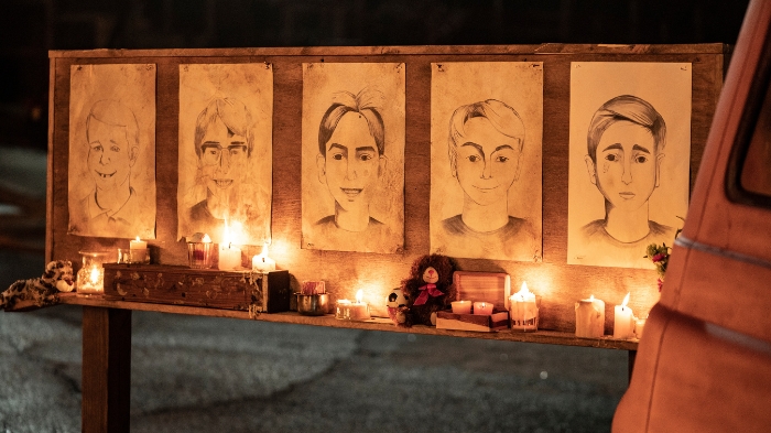Behind-the-Scenes aus The Walking Dead: The Ones Who Live: Eine improvisierte Gedenkstätte mit fünf gezeichneten Porträts auf einer Holztafel, umgeben von brennenden Kerzen, Stofftieren und kleinen Andenken.
