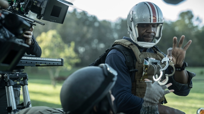 Behind-the-Scenes aus The Walking Dead: The Ones Who Live: Terry Crewes in taktischer Ausrüstung mit Helm hebt die Hand, während ihm jemand Handschellen reicht. Kameras im Vordergrund.