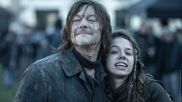 Norman Reedus und eine junge Schauspielerin grinsen in die Kamera.