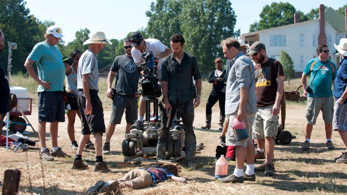 Behind-the-Scenes aus The Walking Dead: Andrew Lincoln (Rick) steht am Set, umgeben von Crewmitgliedern und Kameraausrüstung, während eine Szene mit einem am Boden liegenden Darsteller vorbereitet wird.