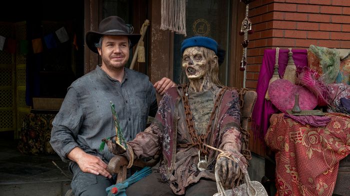 TWD-Set: Josh McDermitt (Eugene) posiert neben einer Walker-Puppe mit blauer Mütze und Ketten.