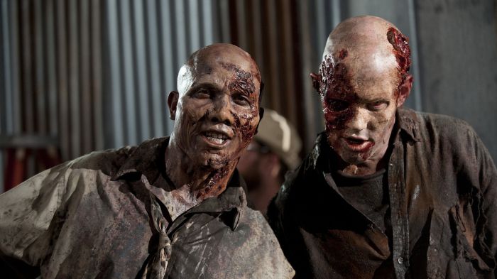 Behind-the-Scenes aus The Walking Dead: Zwei Darsteller in aufwendigem Zombie-Make-up posieren am Set mit realistischen Wunden und blutverschmierter Kleidung.