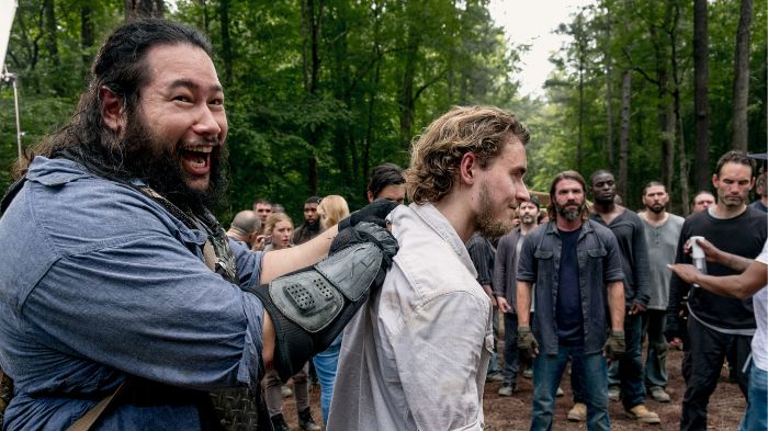 Behind-the-Scenes aus The Walking Dead: Cooper Andrews (Jerry) lacht, während er scherzhaft Macsen Lintz (Henry) an den Schultern hält, umgeben von Statisten in einer Waldszene.