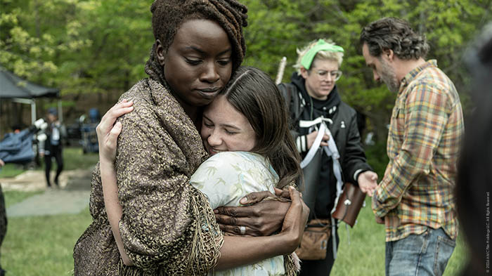 Behind-the-Scenes aus The Walking Dead: The Ones Who Live: Danai Gurira (Michonne) umarmt eine junge Darstellerin herzlich am Set, während Andrew Lincoln (Rick) und Crewmitglieder im Hintergrund zu sehen sind.