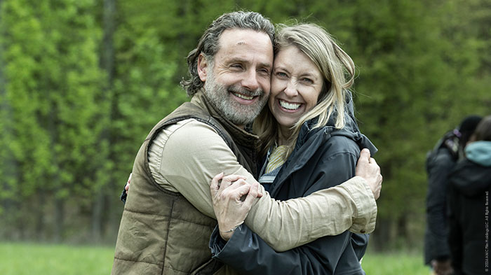 Behind-the-Scenes aus The Walking Dead: The Ones Who Live: Andrew Lincoln (Rick) und eine Crewmitglied-Frau umarmen sich lachend auf einer grünen Wiese.