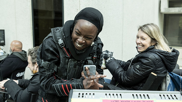Behind-the-Scenes aus The Walking Dead: The Ones Who Live: Danai Gurira (Michonne) in taktischer Ausrüstung lacht, während sie mit einer Crewmitglied-Frau hinter einem Monitor scherzt.