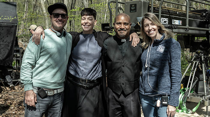 Behind-the-Scenes aus The Walking Dead: The Ones Who Live: Seth Gilliam (Gabriel) und Lesley-Ann Brandt (Pearl) posieren lachend mit zwei Crewmitgliedern vor Kameraequipment im Wald.