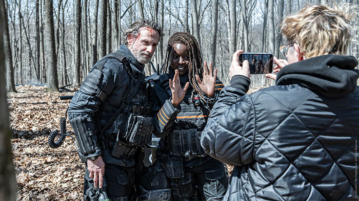 Behind-the-Scenes aus The Walking Dead: The Ones Who Live: Andrew Lincoln (Rick) und Danai Gurira (Michonne) in taktischer Ausrüstung posieren lachend für ein Foto im winterlichen Wald.