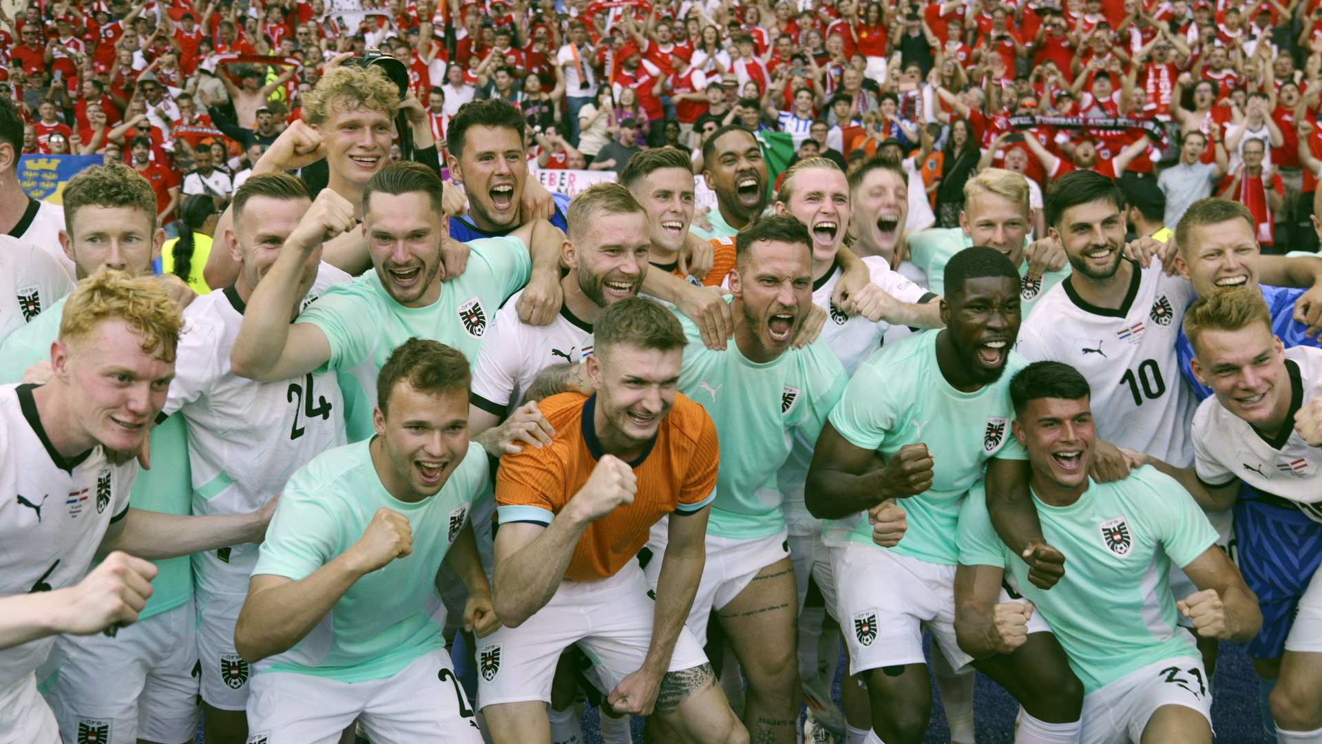 Die österreichische Fußballnationalmannschaft jubelt gemeinsam nach einem erfolgreichen Spiel, umringt von begeisterten Fans in einem Stadion. Die Spieler tragen weiße und mintgrüne Trikots mit dem Wappen des ÖFB.